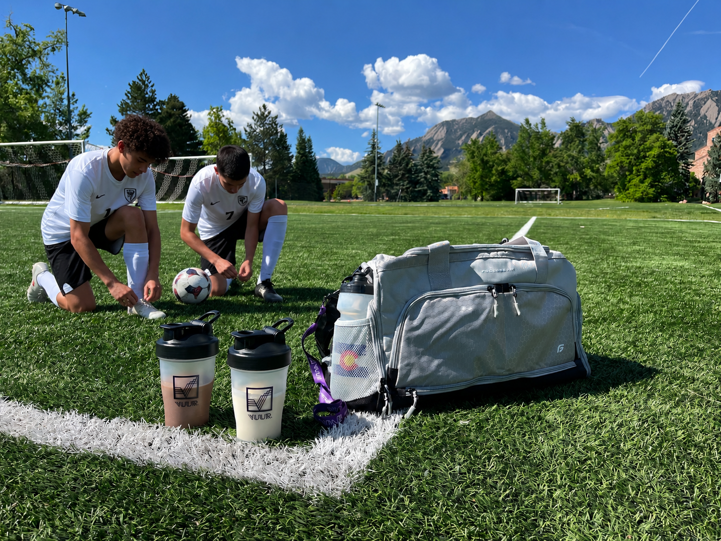 Two teen soccer players preparing to take the field with their VUUR shaker bottles. Colorado mountains in the background. Athletic bag on the ground.