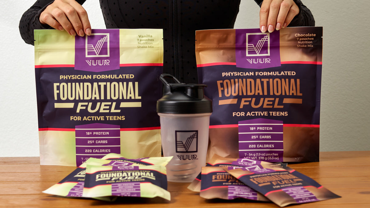 Hands holding two bags of VUUR Foundational Fuel, one Vanilla Flavor and One Chocolate Flavor. In front of these bags are individual pouches of each flavor as well as a shaker bottle.